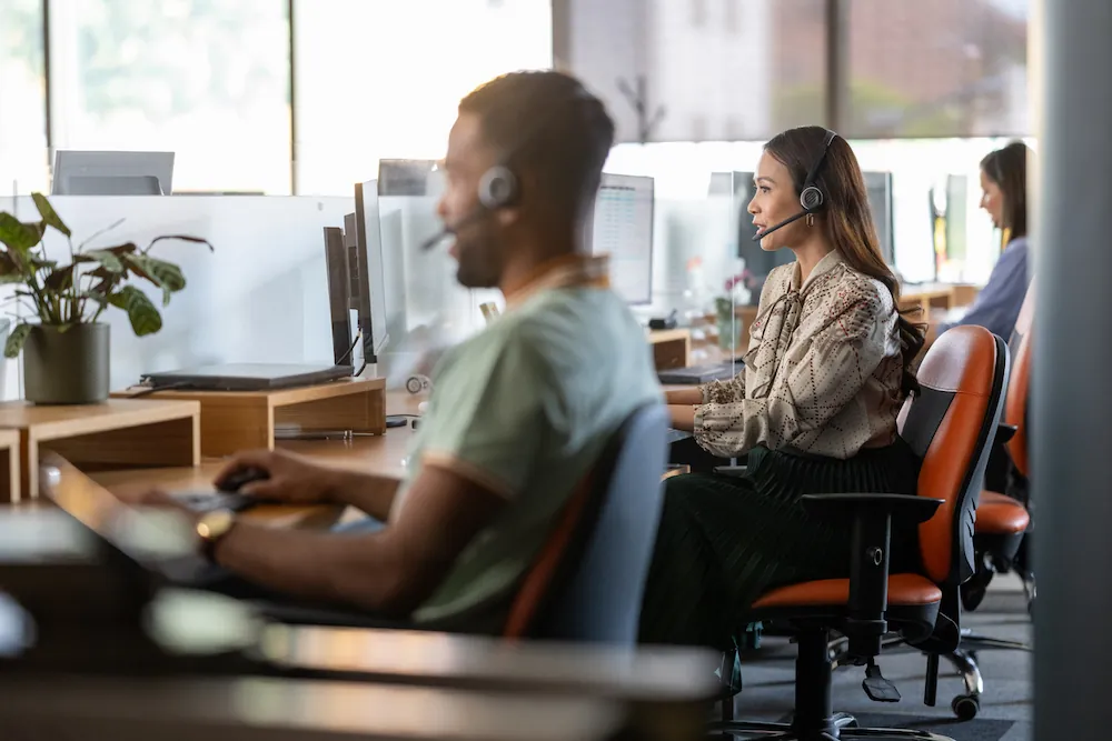 Équipe de support client en centre d'appels avec agents portant des casques, travaillant à leurs postes de travail informatiques dans un bureau moderne.